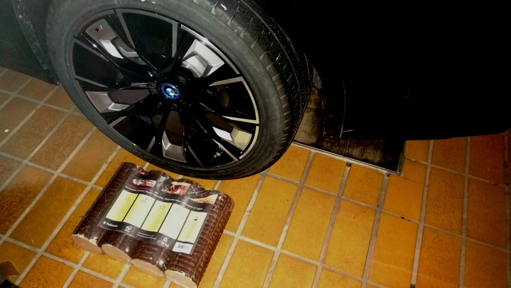 Buchenholzpäckchen mit 4 Stücken und 52 kWh Energiegehalt neben dem Hinterrad vom BMW iX3